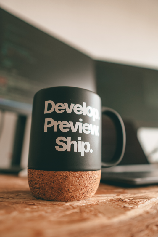 close-up of a black coffee mug with text on it saying: develop. preview. ship.