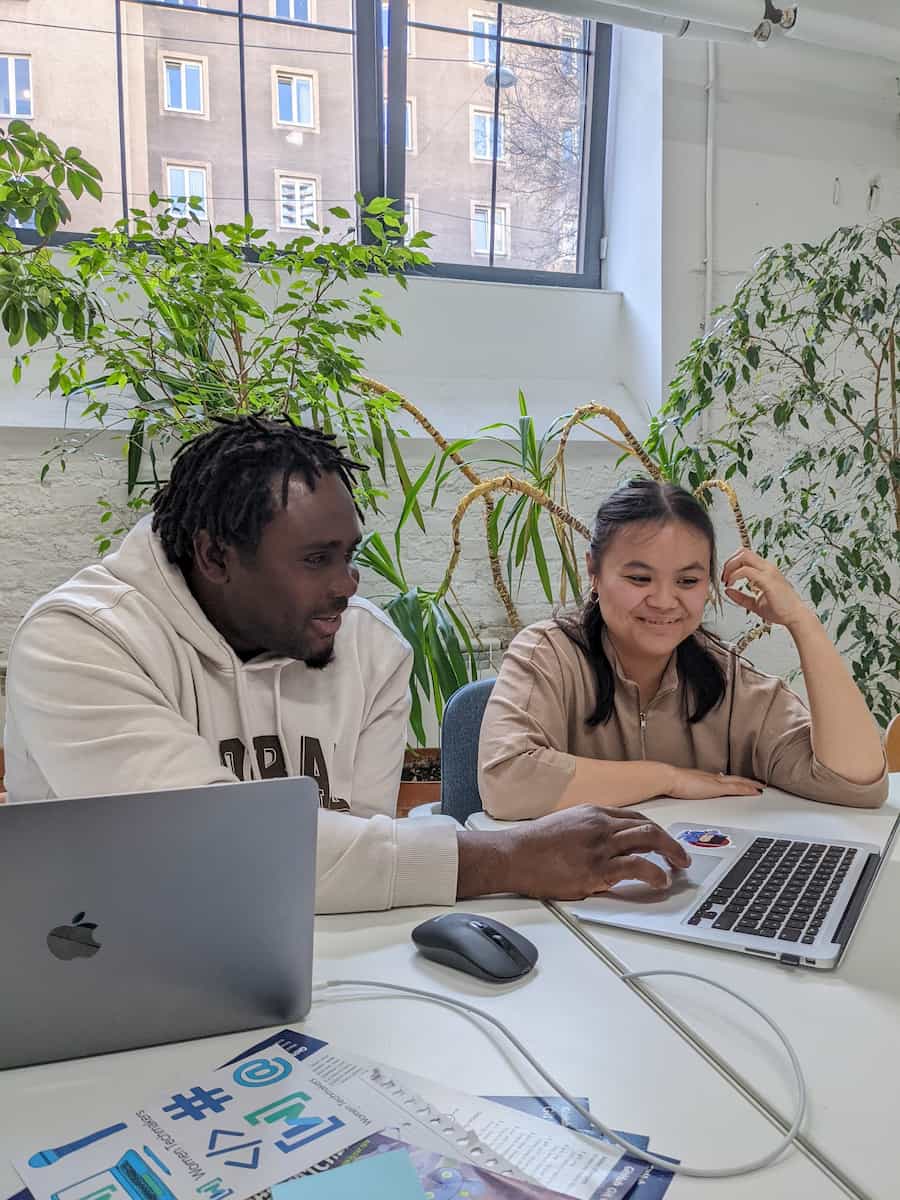 Black male UpLeveled trainer and female student with Asian features, working on laptops, smiling