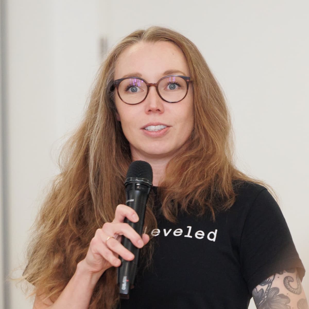 White woman with long hair, wearing glasses and a black shirt talks into a microphone