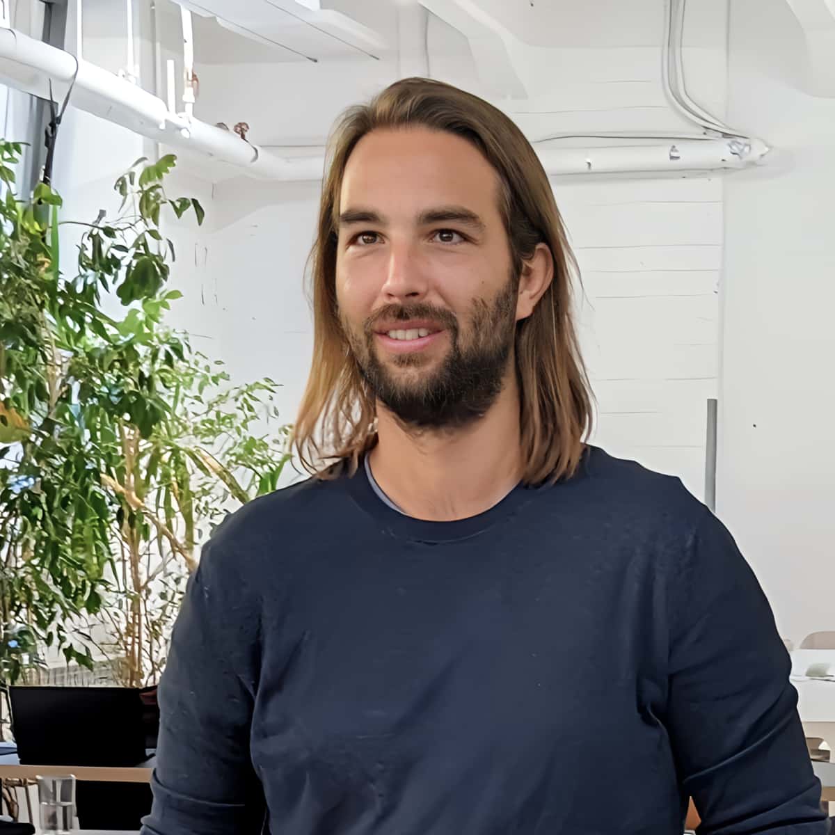Young white man in his thirties, with longer brown hair and a short dark beard, smiling